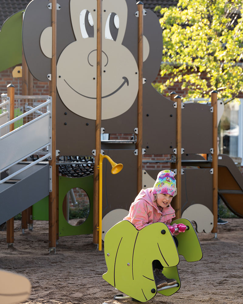 Jungle themed playground, a girl is using an animal shaped rocker, in the background you can see a monkey themed playground unit.